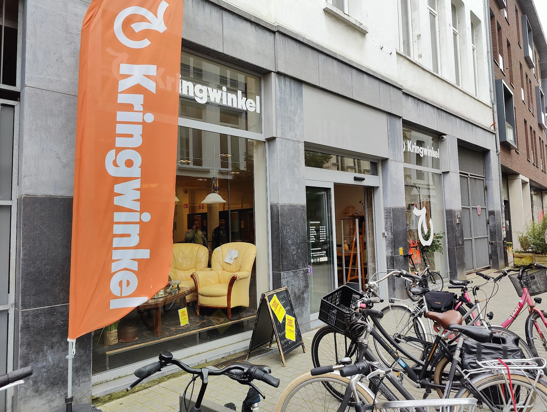 Winkelgevel met oranje banner en gele stoelen in etalage, fietsen geparkeerd ervoor