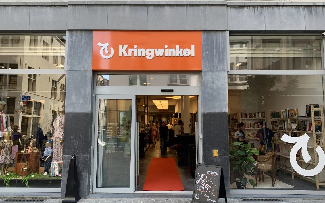 Gevel van kringloopwinkel Kringwinkel met oranje logo, glazen ingang en etalages aan beide zijden