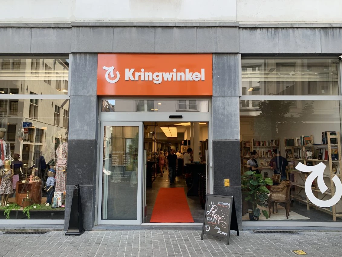 Gevel van kringloopwinkel Kringwinkel met oranje logo, glazen ingang en etalages aan beide zijden