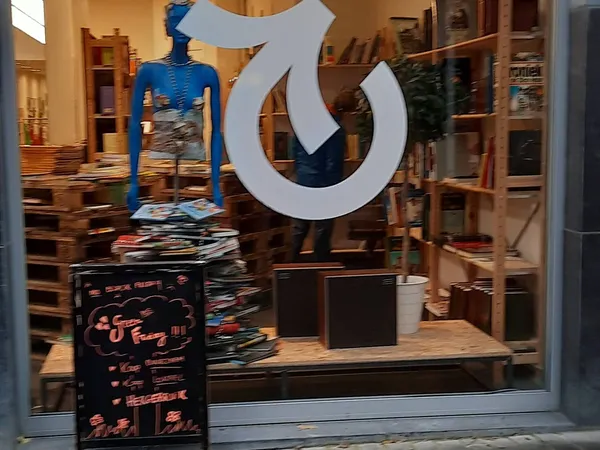 Winkelinterieur met blauwe mannequin, houten stellingen, uitgestalde kleding en groot wit logo op de ruit