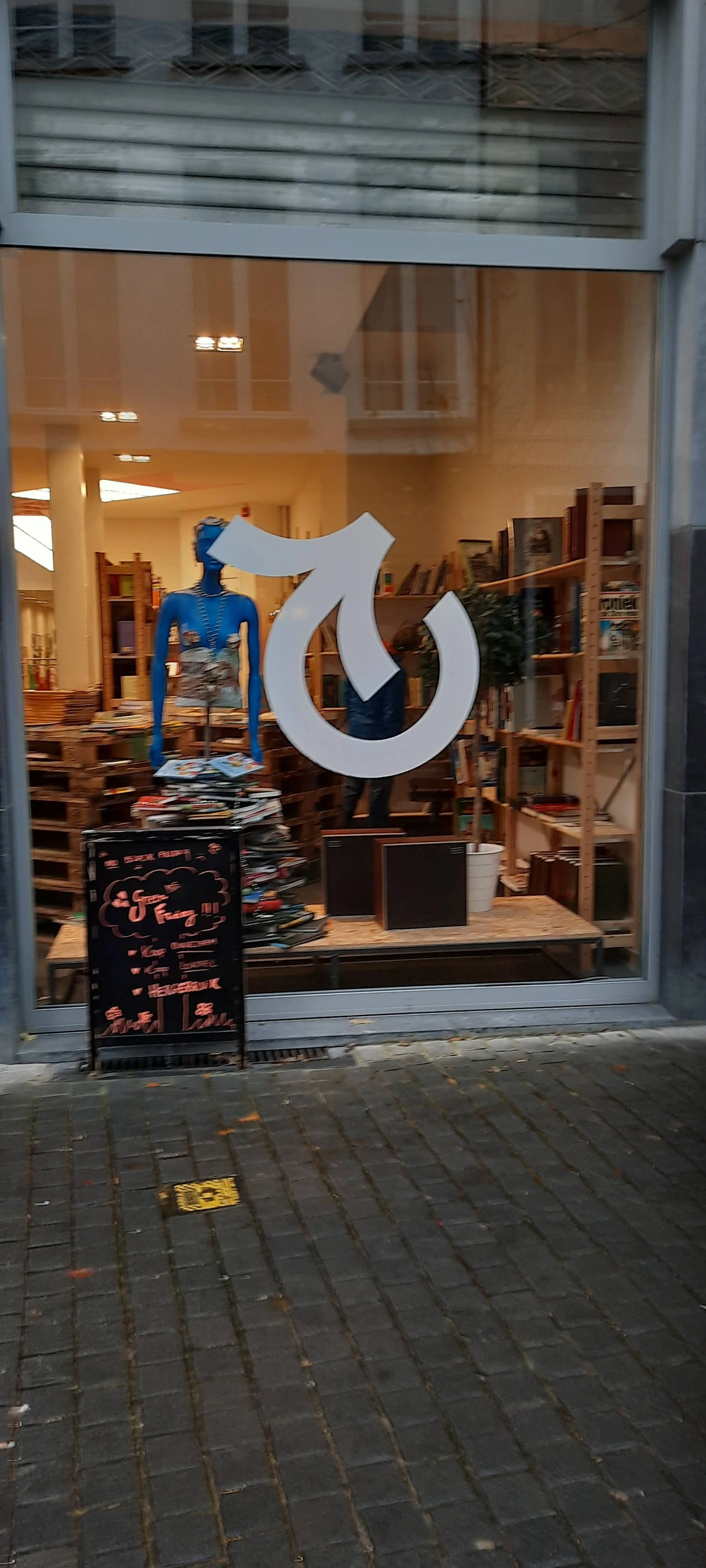 Winkelinterieur met blauwe mannequin, houten stellingen, uitgestalde kleding en groot wit logo op de ruit