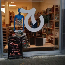 Winkelinterieur met blauwe mannequin, houten stellingen, uitgestalde kleding en groot wit logo op de ruit