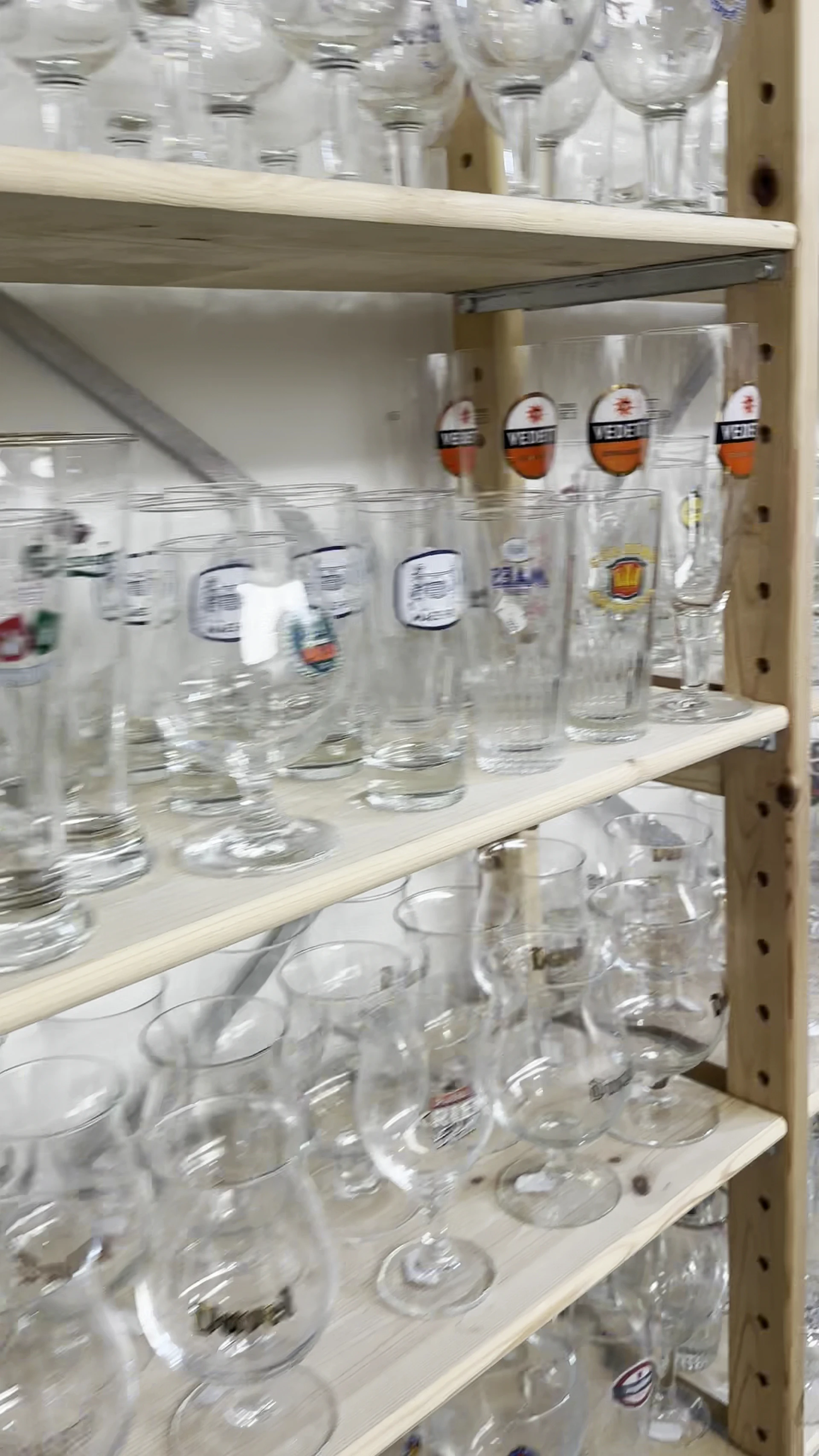 Stellingkast met diverse glazen en drinkglazen met labels, gedeeltelijk scherp in beeld