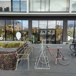 Voorkant van de kringloopwinkel met grote glazen deuren, plantenbakken en fietsenrek op het terras