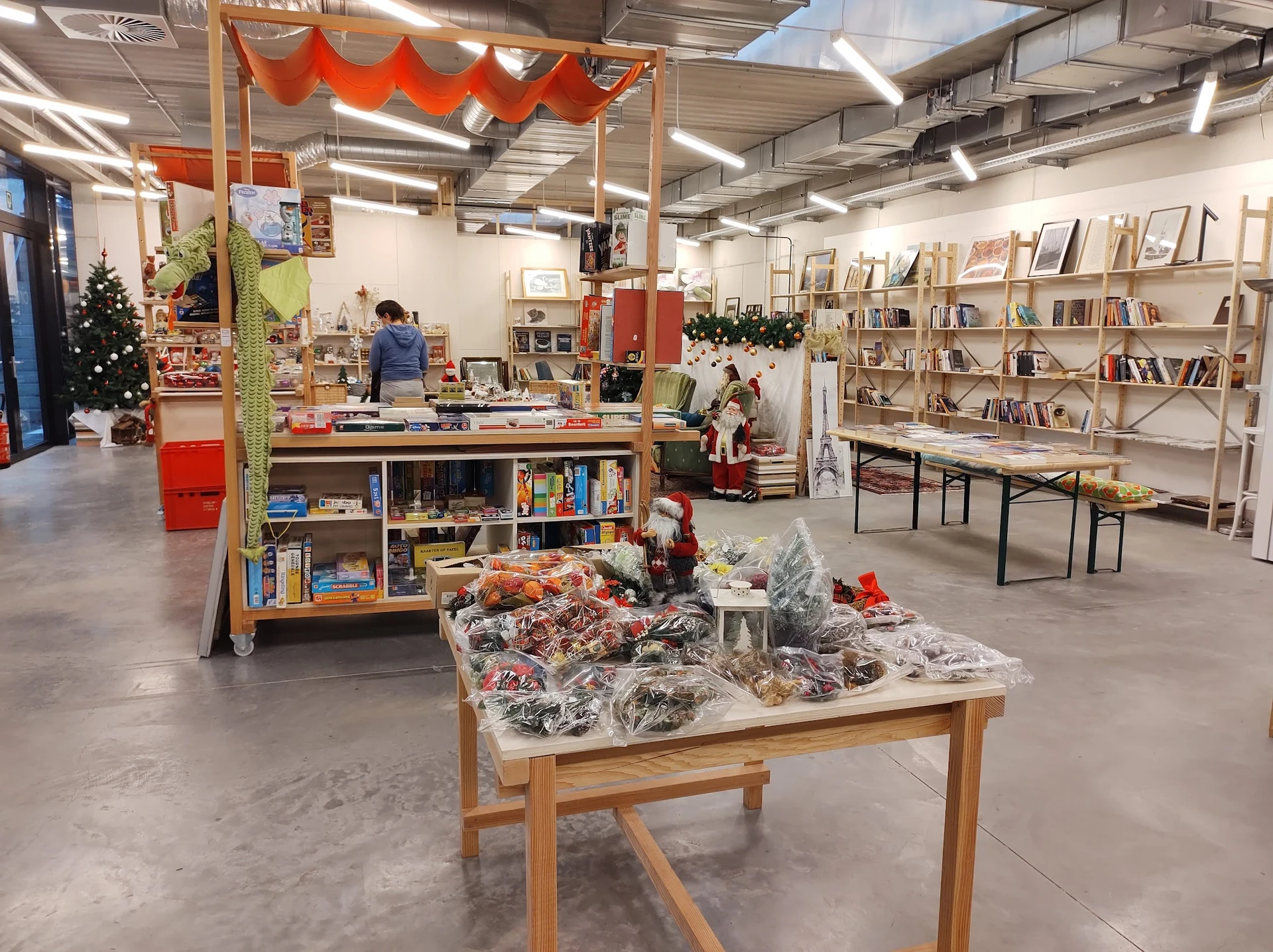 Winkelvloer van kringloopwinkel met boekenkasten, tafels met tweedehands spullen en rode decoratie aan plafond