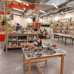 Winkelvloer van kringloopwinkel met boekenkasten, tafels met tweedehands spullen en rode decoratie aan plafond