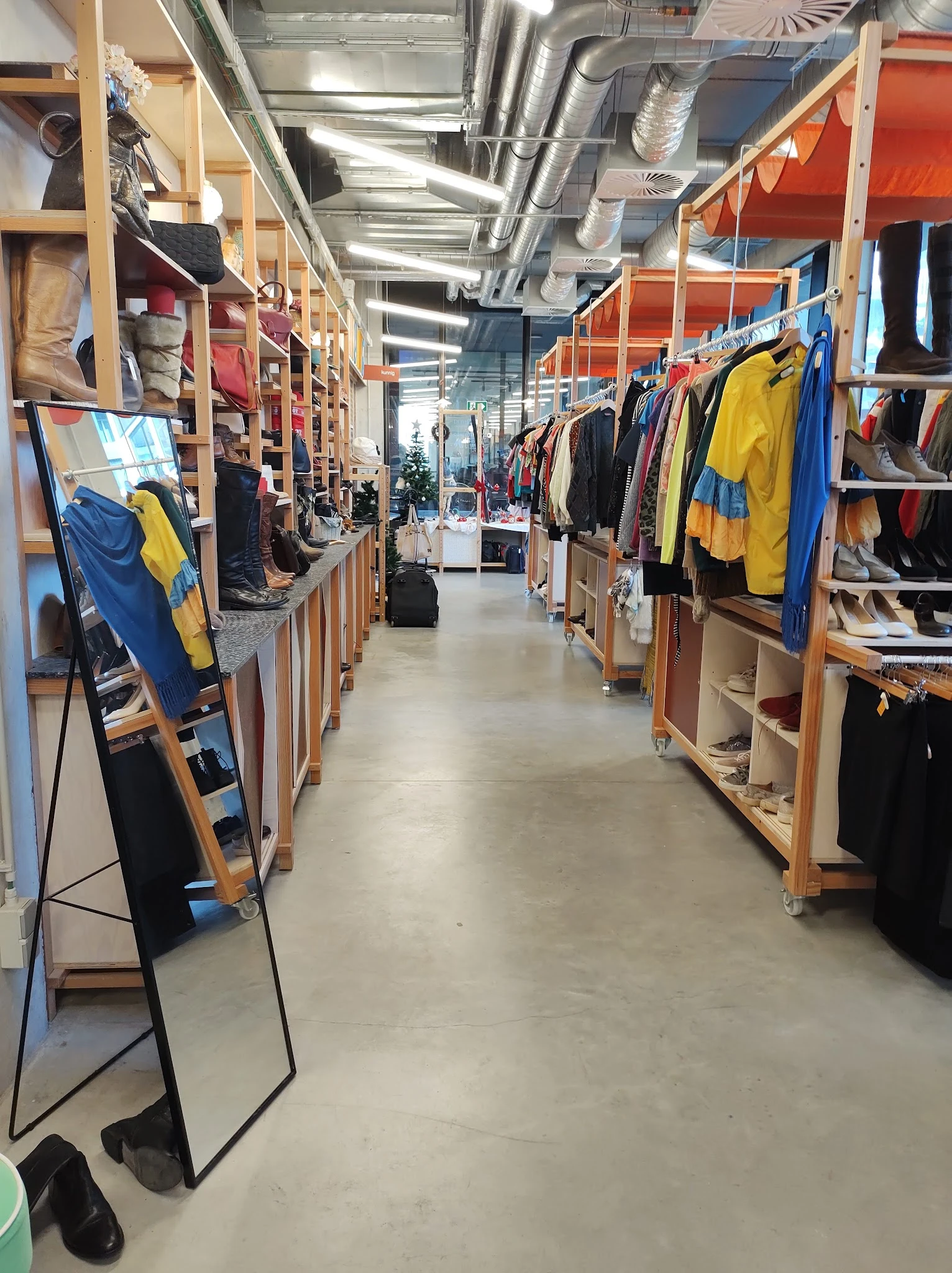 Winkelpad met houten kledingrekken aan weerszijden, volgehangen met tweedehands kleding in verschillende kleuren