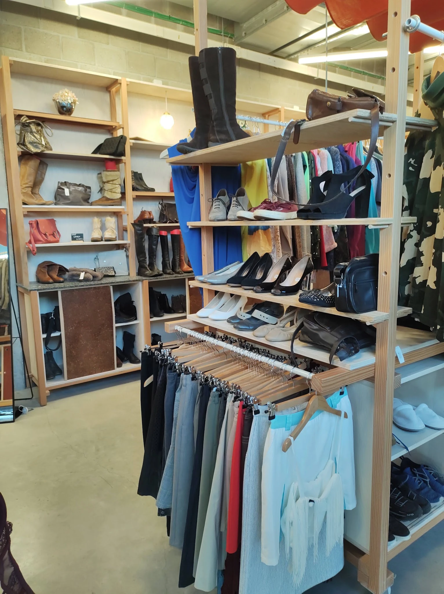 Houten stellingrekken met tweedehands kleding, schoenen, tassen en accessoires netjes uitgestald