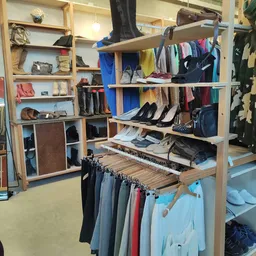 Houten stellingrekken met tweedehands kleding, schoenen, tassen en accessoires netjes uitgestald