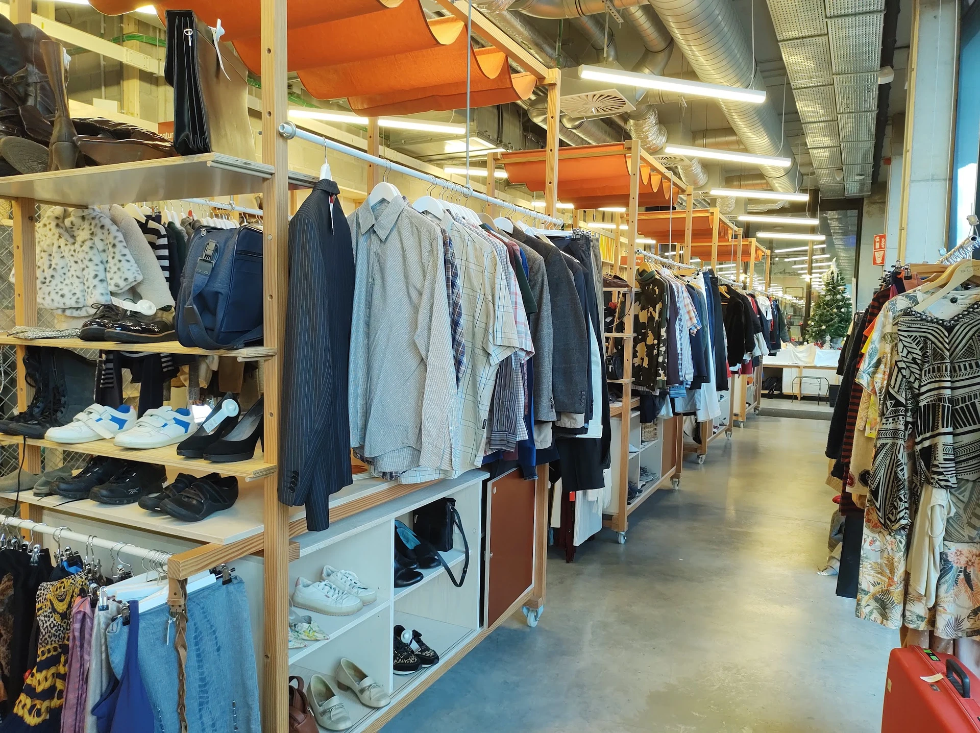 Winkelinterieur met houten stellingen vol tweedehands kleding, schoenen en accessoires langs een gangpad