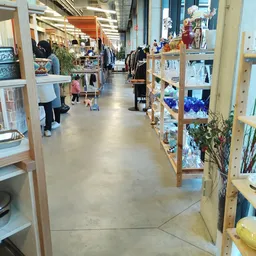 Winkelgang met houten stellingen vol spullen aan beide zijden, enkele bezoekers in de kringloopwinkel