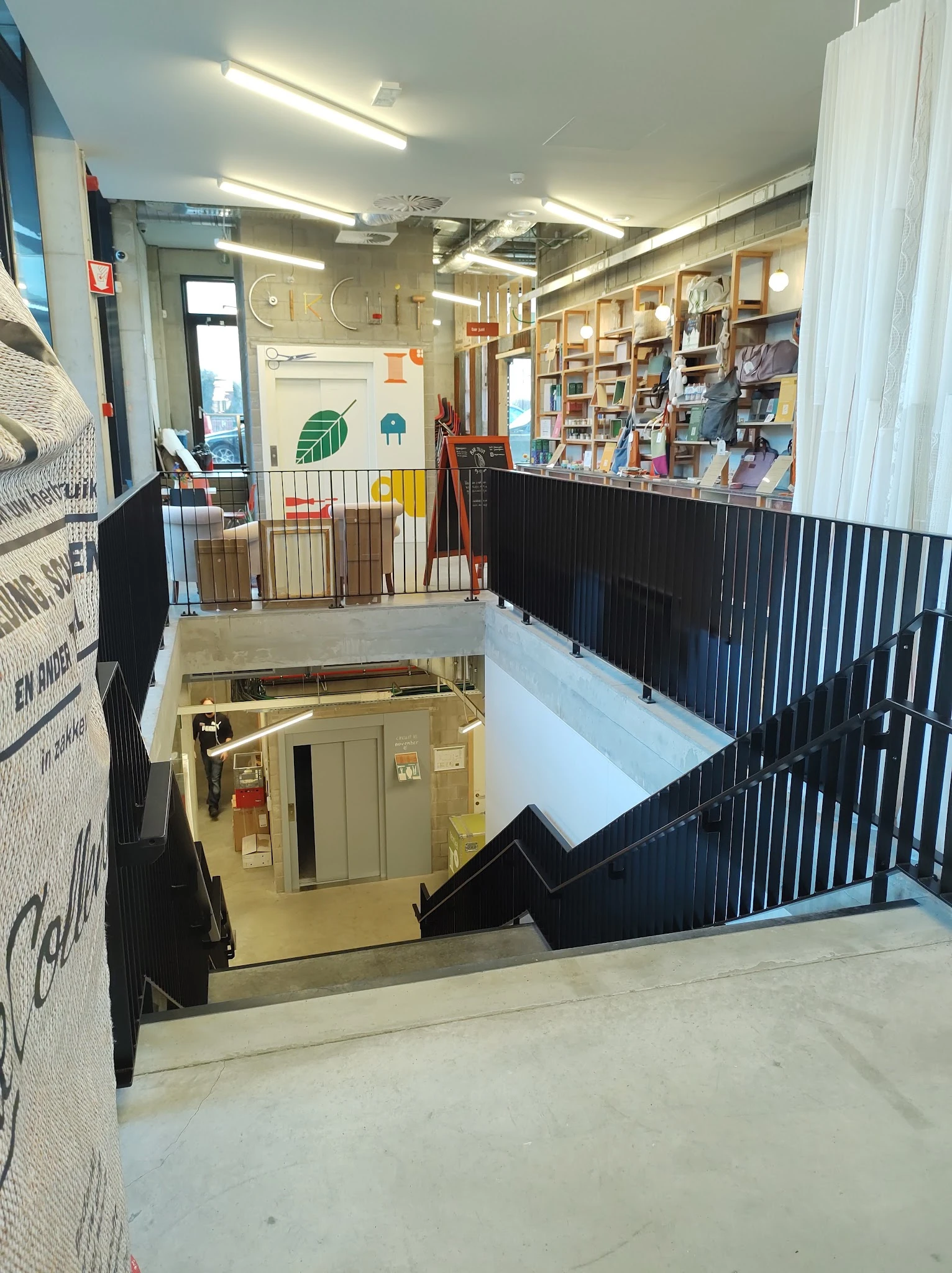 Overzicht van twee verdiepingen in een kringloopwinkel met trappen, zwarte balustrades en boekenkasten