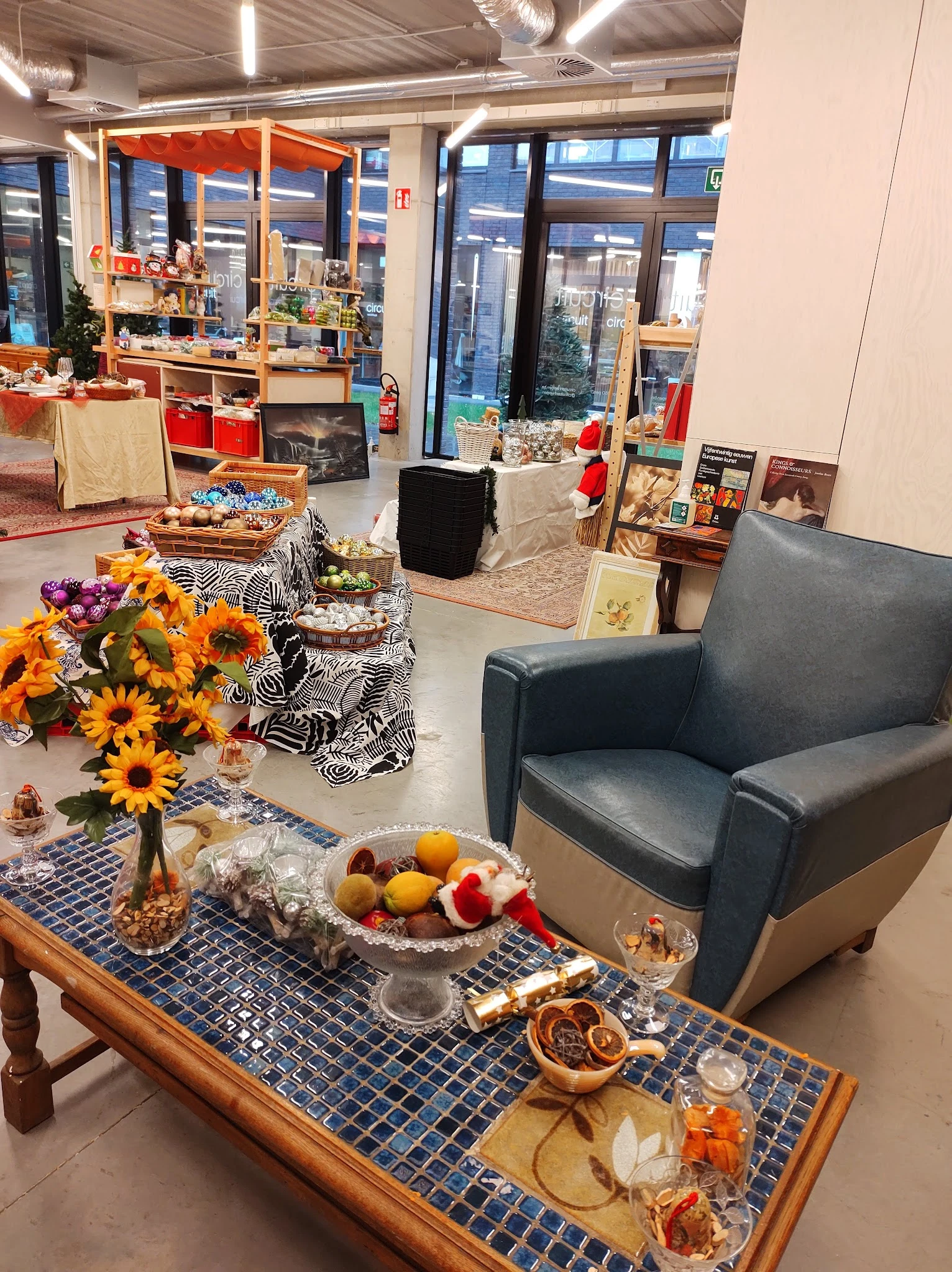Winkelvloer met zithoek, bloemen in vaas, fruit op tafel en diverse meubels en huisraad op achtergrond