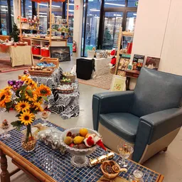 Winkelvloer met zithoek, bloemen in vaas, fruit op tafel en diverse meubels en huisraad op achtergrond