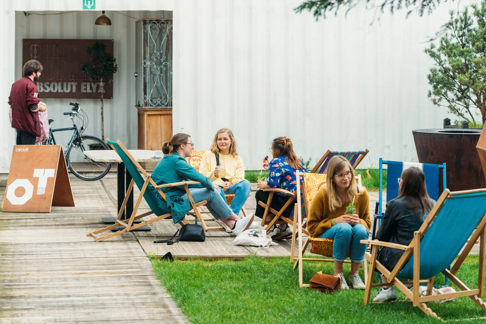 Bezoekers zitten op stoelen op een terras buiten de winkel, sommigen met drankjes