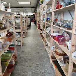 Lange doorgang tussen houten stellingen vol huishoudspullen, vazen, servies en diverse gebruiksartikelen in kringloopwinkel