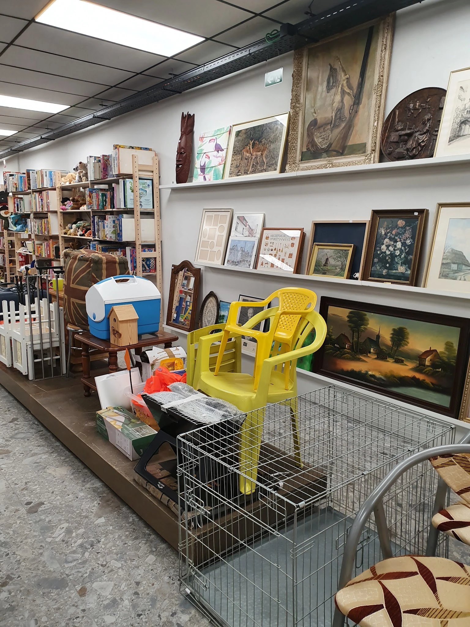 Winkelrek met gele stoelen, kunstwerken, boeken en diverse tweedehandsartikelen op uitstalling