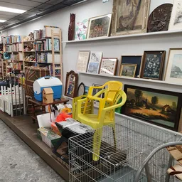 Winkelrek met gele stoelen, kunstwerken, boeken en diverse tweedehandsartikelen op uitstalling