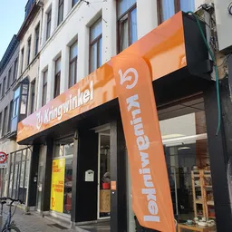 Oranje gevel van kringloopwinkel met grote naam en logo, winkelpui met etalage en ingang zichtbaar