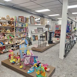 Winkelvloer met speelgoed en boeken op uitstallingstafels, boekenrekken tegen de muur en fietsen op de achtergrond