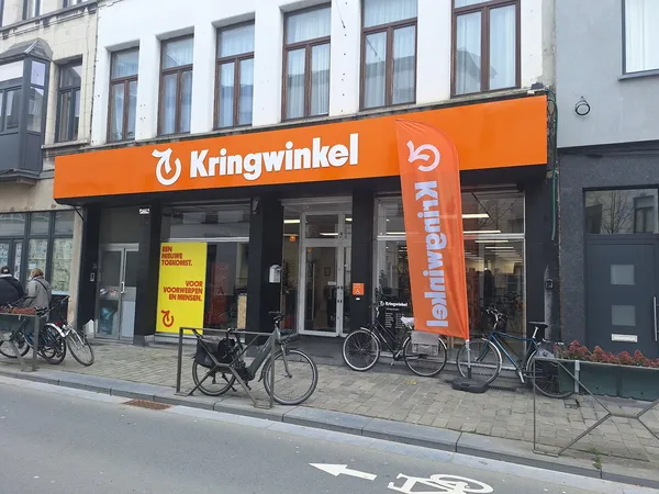 Oranje gevel van kringloopwinkel met grote ramen en uithangteksten, fietsen geparkeerd voor de ingang