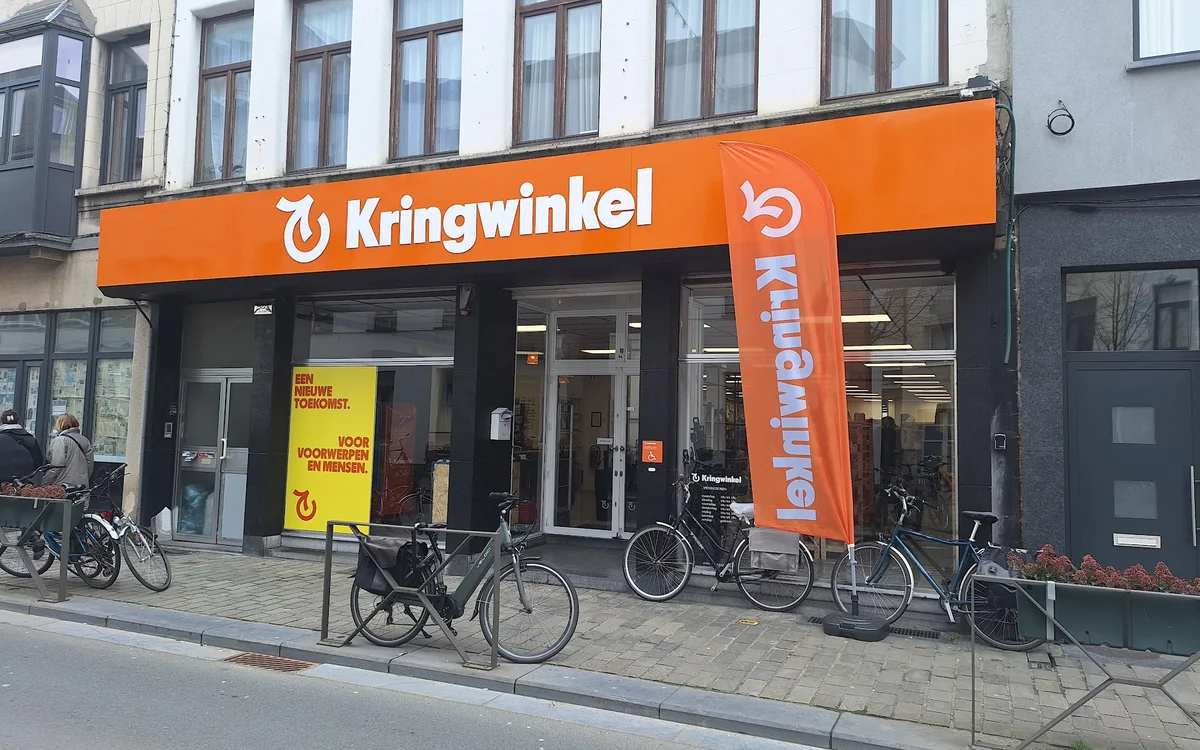 Oranje gevel van kringloopwinkel met grote ramen en uithangteksten, fietsen geparkeerd voor de ingang