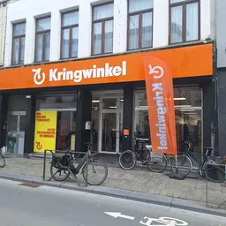 Oranje gevel van kringloopwinkel met grote ramen en uithangteksten, fietsen geparkeerd voor de ingang