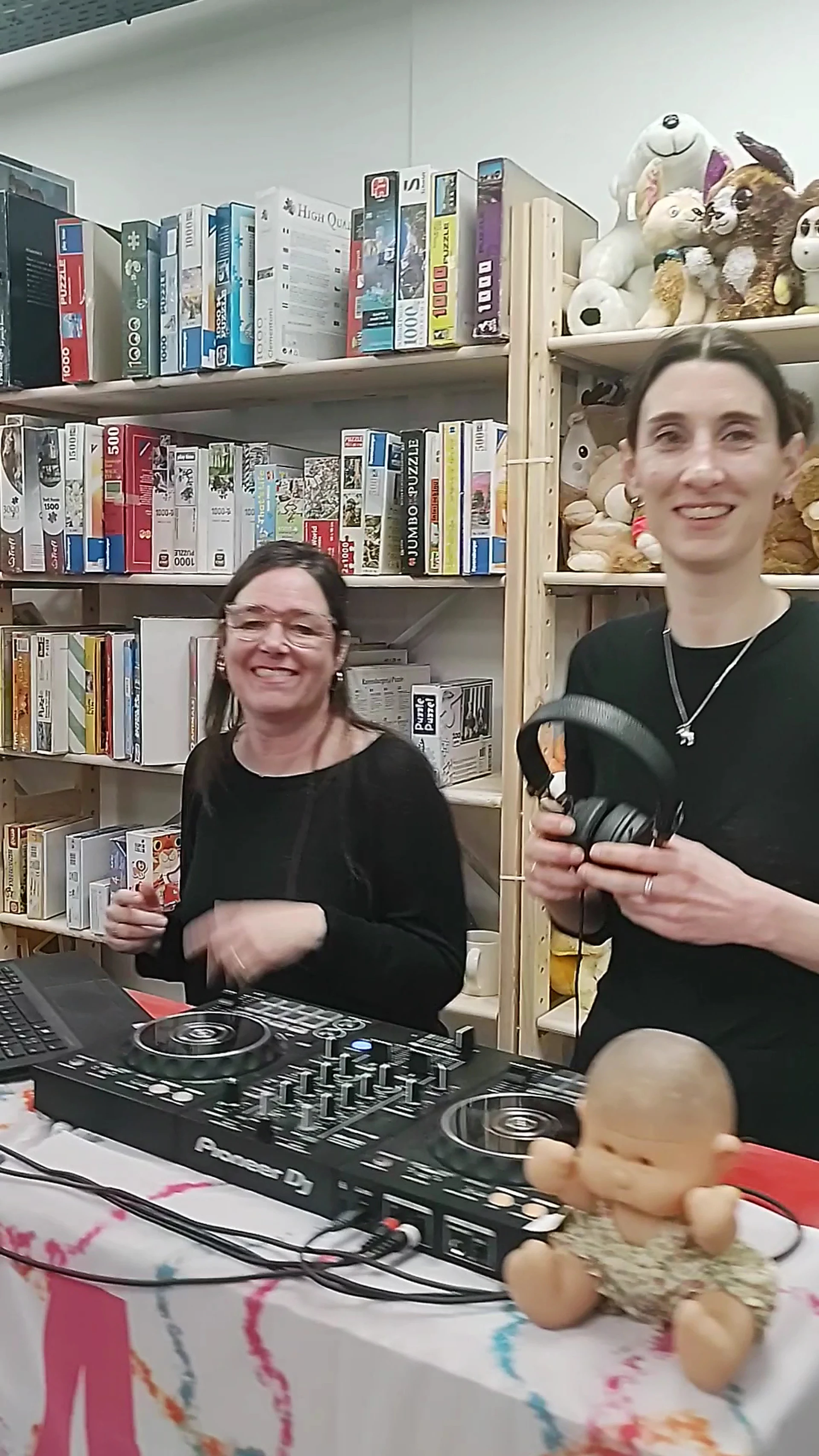 Twee medewerkers in de kringwinkel presenteren koptelefoons en ander materiaal voor camera