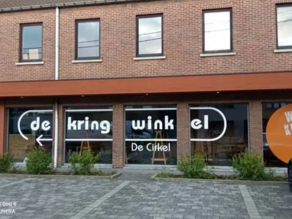 Gevel van kringloopwinkel met bakstenen voorgevel, grote ramen en zwarte uithangtekst met winkelnaam