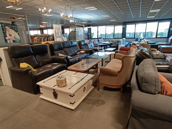 Winkelvloer met meubels: zwarte lederen bank, beige fauteuils, witte kist als salontafel, grote ramen op achtergrond