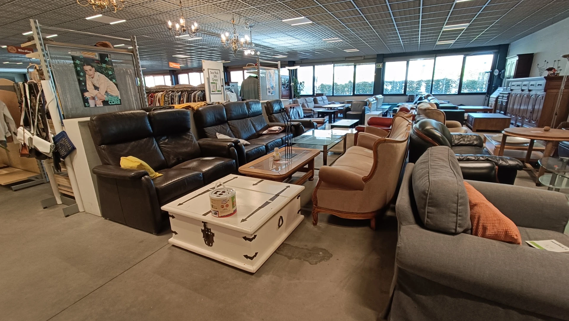 Winkelvloer met meubels: zwarte lederen bank, beige fauteuils, witte kist als salontafel, grote ramen op achtergrond