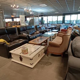 Winkelvloer met meubels: zwarte lederen bank, beige fauteuils, witte kist als salontafel, grote ramen op achtergrond