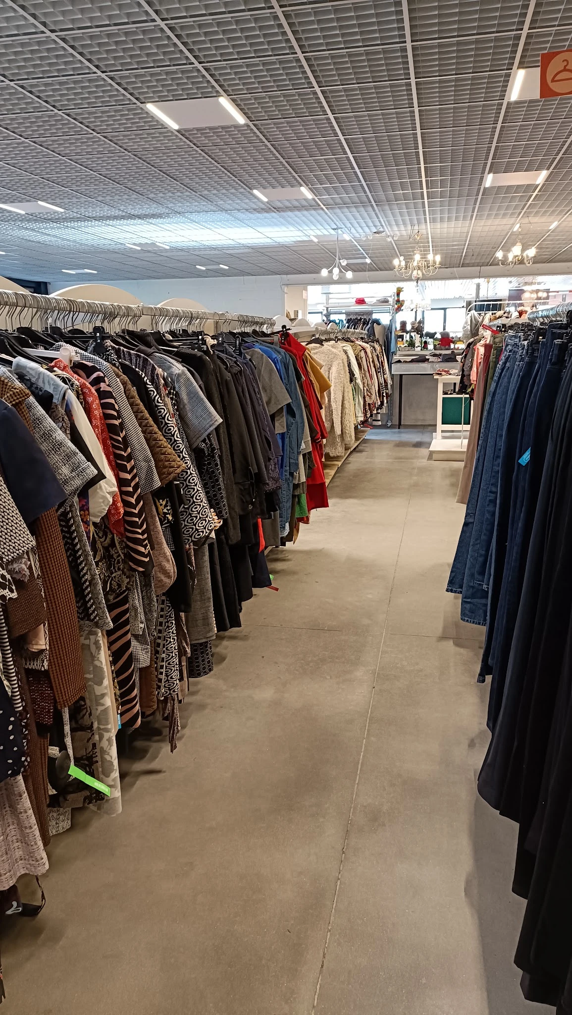 Rekken met tweedehands kleding, waaronder jassen, jasjes en truien in verschillende kleuren en patronen