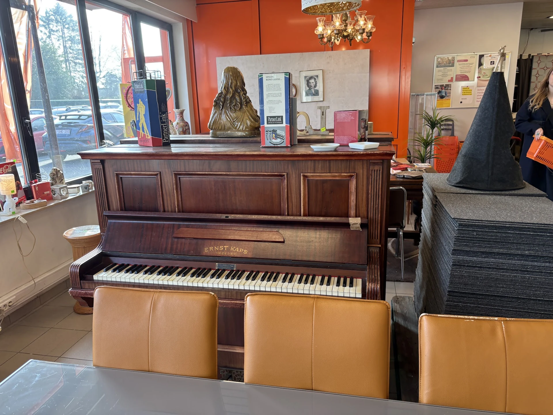 Bruine houten piano met gele zitbanken eronder in een kringloopwinkel