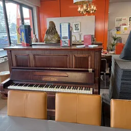 Bruine houten piano met gele zitbanken eronder in een kringloopwinkel