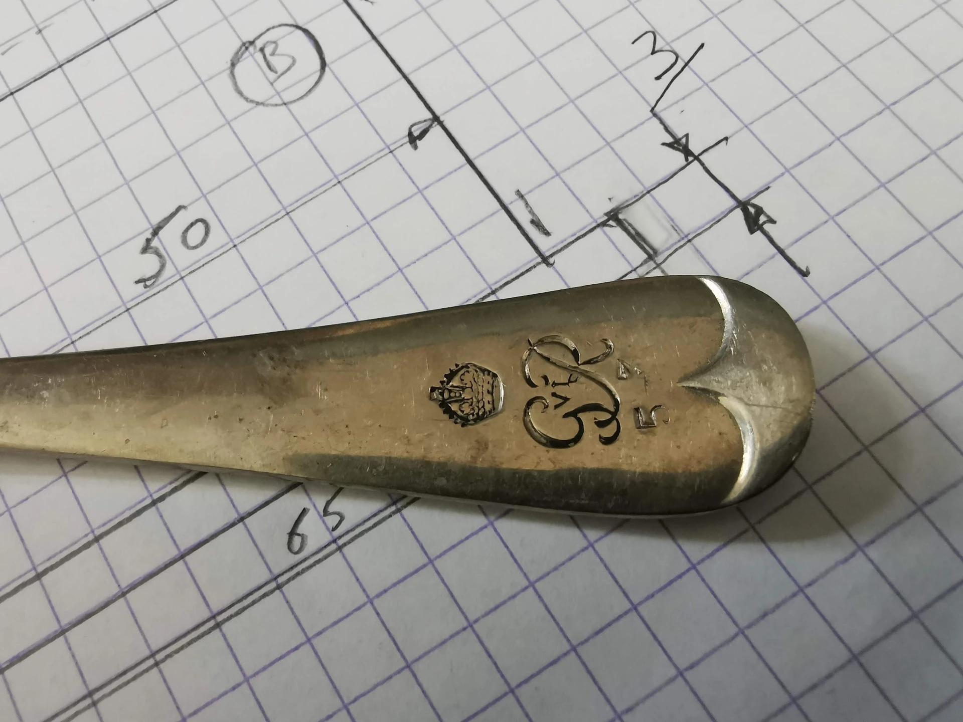 Close-up van een antieke messing lepel met gravering op ruitjespapier met aantekeningen