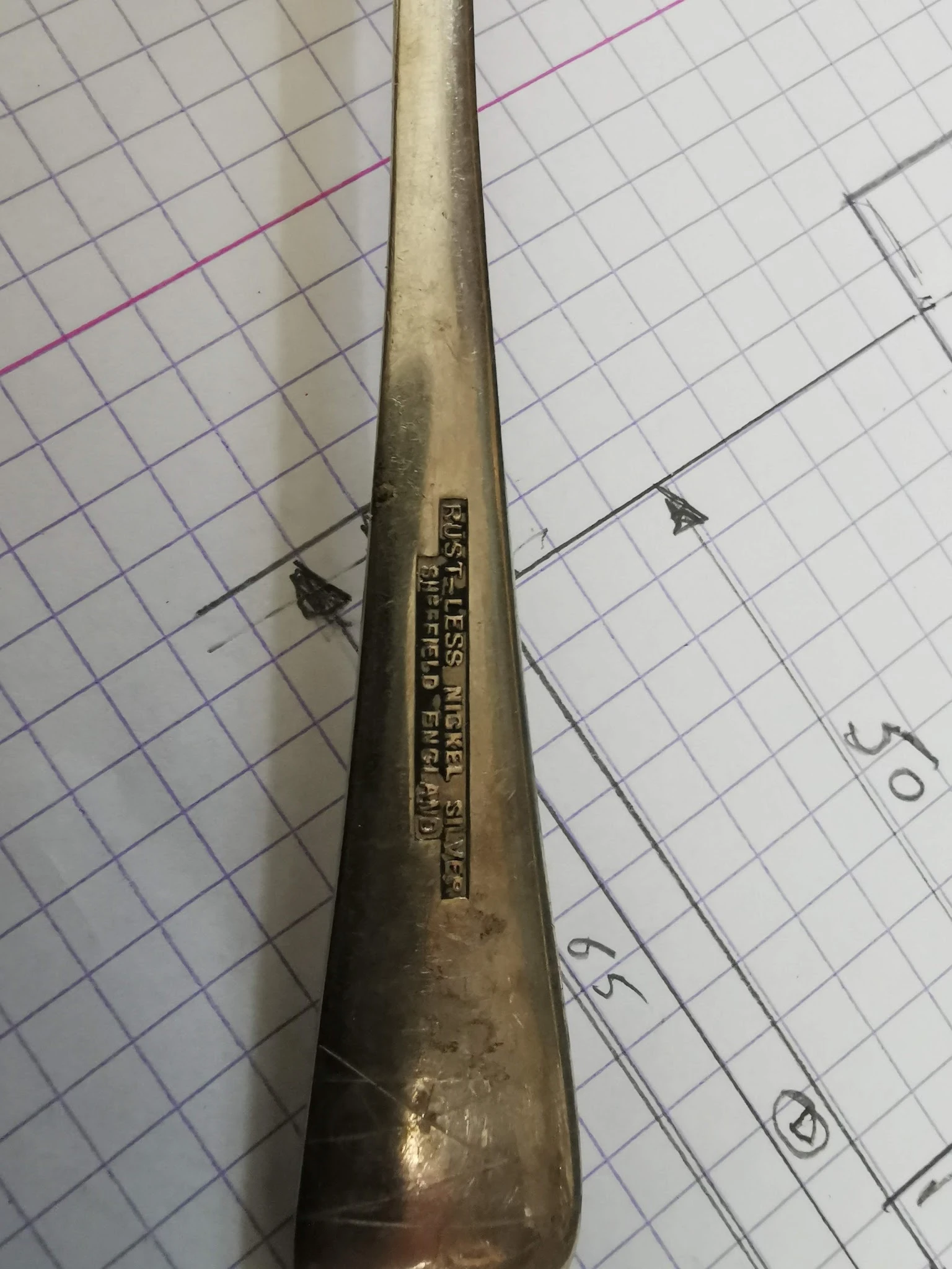 Close-up van een oude metalen buissleutel of spuitbus met ingegraveerde tekst, op ruitjespapier.