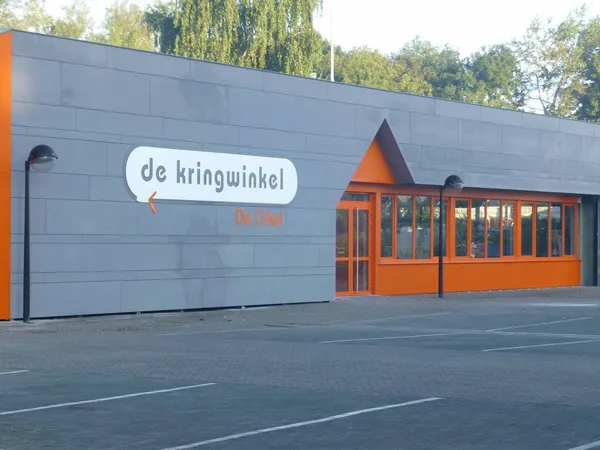 Grijze gevel van kringloopwinkel met oranje accenten en winkelnaam 'de kringwinkel' op bord