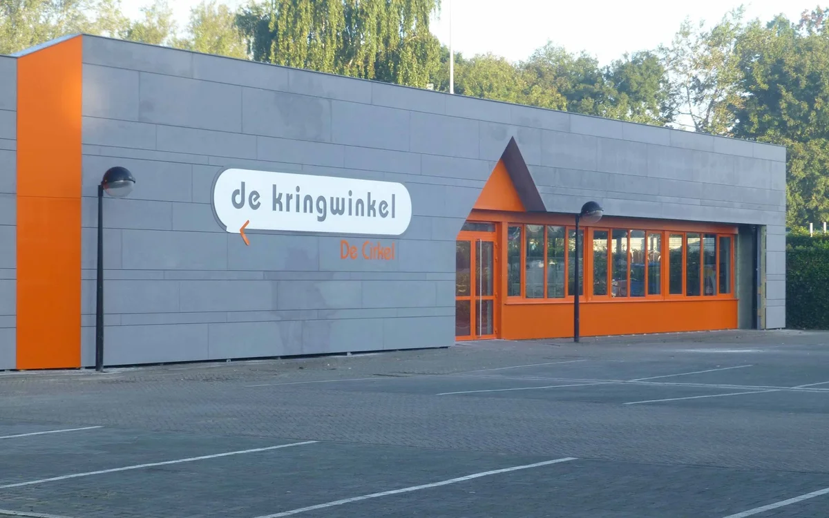 Grijze gevel van kringloopwinkel met oranje accenten en winkelnaam 'de kringwinkel' op bord