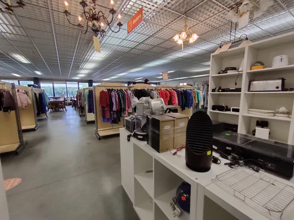 Winkelvloer van kringloopwinkel met kledingrekken, witte kastjes en winkelafdelingen