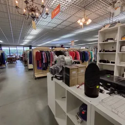 Winkelvloer van kringloopwinkel met kledingrekken, witte kastjes en winkelafdelingen