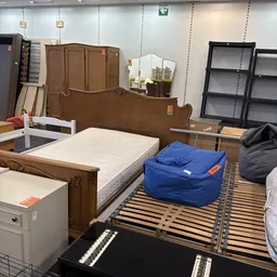 Tweedehands meubelen in een kringloopwinkel: houten bed, matras, blauwe poef en kasten op stellingen