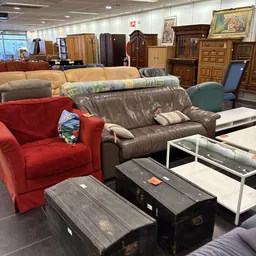 Tweedehands meubels in de winkel: rode fauteuil, grijze bank en ander interieur
