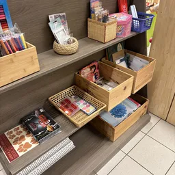 Houten opbergboxen en manden met diverse artikelen zoals notitieboeken, papier en kantoorspullen op een grijze houten kast