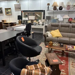 Winkelvloer met meubels: grijze bank, zwarte bureaustoel, houten tafel en diverse lampen en decoratie