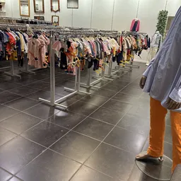 Winkelinterieur met meerdere rekken vol tweedehands kleding op hangers tegen donkere tegelvloer