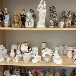 Twee schappen met wit porselein en decoratieve items zoals beeldjes, vazen en servies