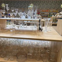 Uitgestalde kristallen glazen en serviesgoed op toonbanken in een kringloopwinkel