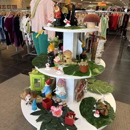Drielaags displaystandaard met tuinkabouters, planten, bloemen en decoratieve items in kringloopwinkel