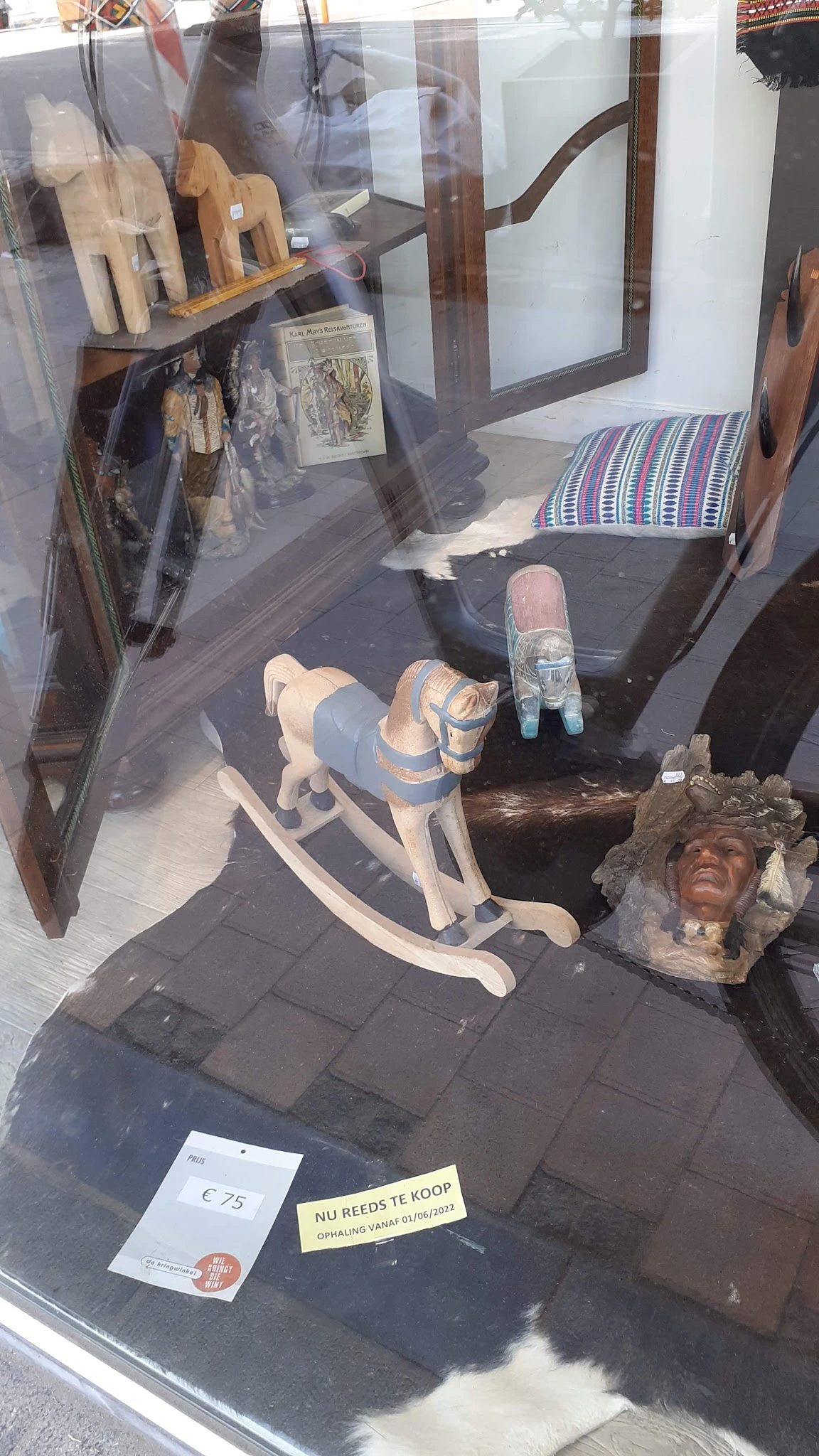 Diverse tweedehands items op de vloer: houten beeldje, sculptuur, schoenen en andere huishoudelijke spullen